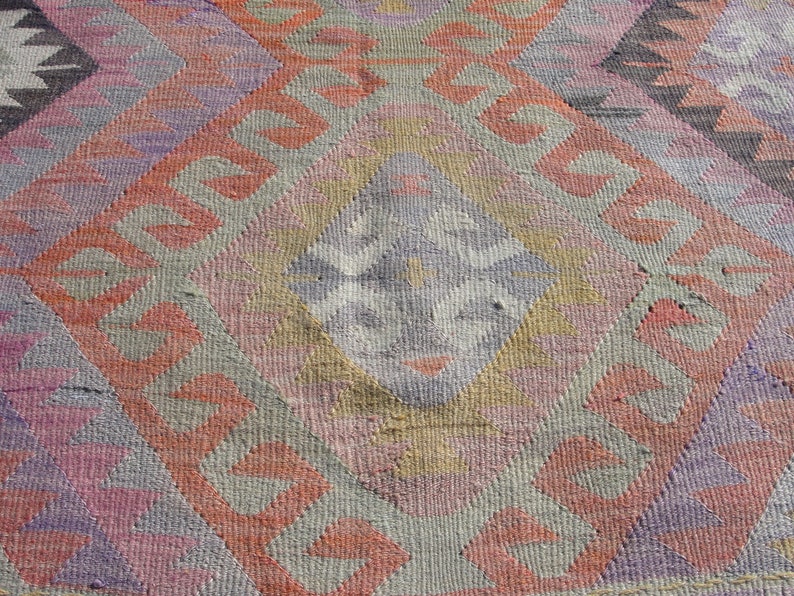 K&ouml;nnte beinhalten: Eine Nahaufnahme eines bunten gewebten Teppichs mit geometrischem Muster. Der Teppich ist aus Wolle und hat eine Vielzahl von Farben, darunter Rosa, Rot, Lila und Grau.