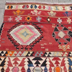 May include: A red, black, and white patterned rug with geometric designs. The rug has a central medallion with a starburst pattern and two smaller medallions with geometric shapes.