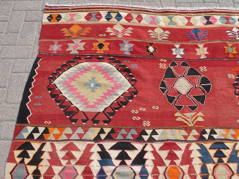 May include: A red, black, and white patterned rug with geometric designs. The rug has a central medallion with a starburst pattern and two smaller medallions with geometric shapes.