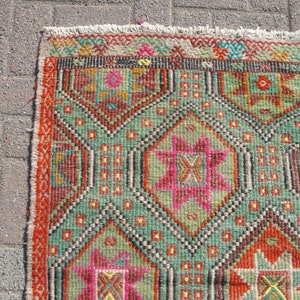 Puede incluir: Una alfombra colorida con un patr&oacute;n geom&eacute;trico en tonos rojos, verdes, rosas y amarillos. La alfombra tiene un borde de flecos.