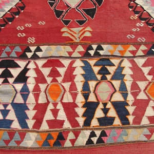 May include: Close-up of a colorful woven rug with a geometric pattern. The rug features a variety of colors, including red, blue, white, and orange. The pattern is made up of triangles, diamonds, and other shapes.