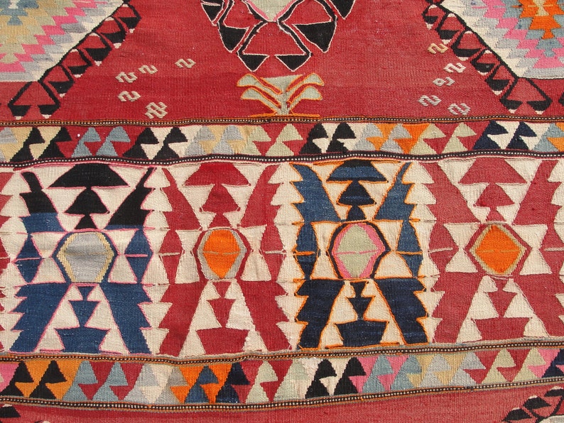 May include: Close-up of a colorful woven rug with a geometric pattern. The rug features a variety of colors, including red, blue, white, and orange. The pattern is made up of triangles, diamonds, and other shapes.