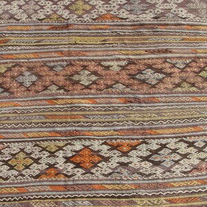 K&ouml;nnte beinhalten: Nahaufnahme eines gewebten Teppichs mit geometrischem Muster. Der Teppich weist eine Mischung aus Braun-, Orange- und Cremefarben mit komplizierten Diamant- und Streifendesigns auf. Die Textur des Teppichs ist sichtbar.