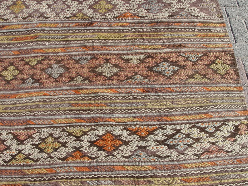 K&ouml;nnte beinhalten: Nahaufnahme eines gewebten Teppichs mit geometrischem Muster. Der Teppich weist eine Mischung aus Braun-, Orange- und Cremefarben mit komplizierten Diamant- und Streifendesigns auf. Die Textur des Teppichs ist sichtbar.