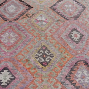 K&ouml;nnte beinhalten: Ein bunter Teppich mit einem geometrischen Muster in Rosa-, Orange-, Grau- und Schwarzt&ouml;nen. Der Teppich hat ein traditionelles Design mit sich wiederholenden Diamantenformen und filigranen Details.