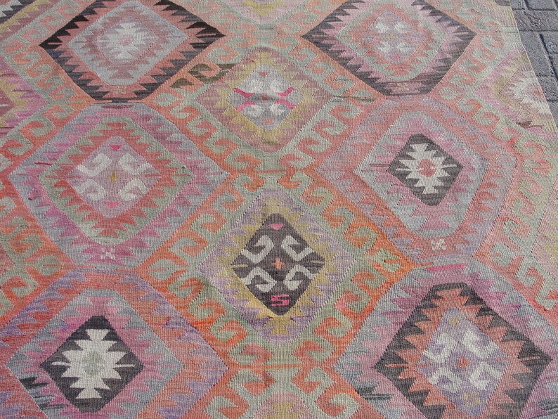 K&ouml;nnte beinhalten: Ein bunter Teppich mit einem geometrischen Muster in Rosa-, Orange-, Grau- und Schwarzt&ouml;nen. Der Teppich hat ein traditionelles Design mit sich wiederholenden Diamantenformen und filigranen Details.