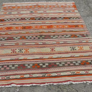 May include: A rectangular, hand-woven rug with a striped pattern in shades of orange, red, brown, and cream. The rug features geometric designs and fringe along the edges. The rug measures approximately 60 inches by 90 inches.
