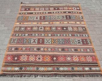 May include: A traditional Turkish kilim rug with a geometric pattern in shades of red, brown, beige, and white. The rug has a fringe border.