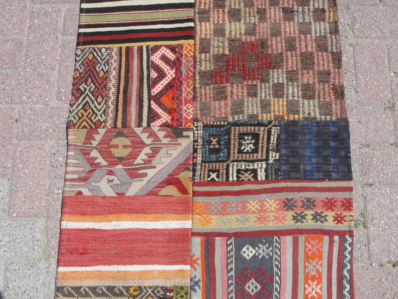 May include: A patchwork rug made of different colored fabrics with geometric patterns. The rug is made up of nine squares, each with a different design. The rug is a mix of red, orange, brown, blue, and white.