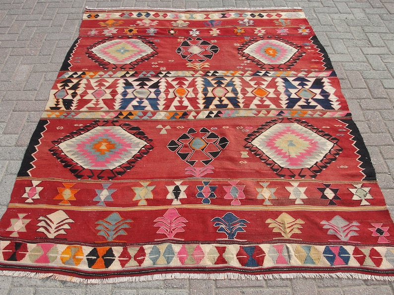 May include: A red, black, white, blue, and pink patterned rug with a geometric design. The rug has a fringe border.