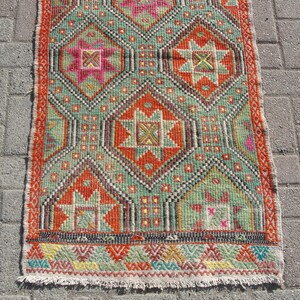 Puede incluir: Una alfombra kilim turca tradicional con un patr&oacute;n geom&eacute;trico en tonos rojos, verdes, naranjas y amarillos. La alfombra tiene un borde de flecos y est&aacute; hecha de lana.