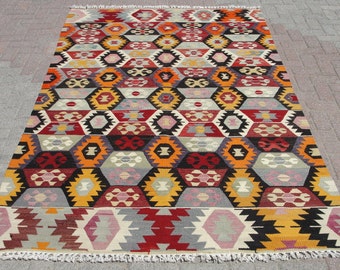 May include: A colorful geometric patterned rug with a fringe border. The rug features a repeating pattern of hexagons and triangles in shades of red, orange, yellow, black, and gray.