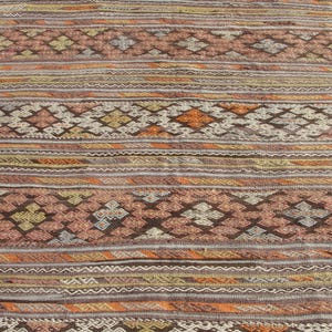 K&ouml;nnte beinhalten: Ein rechteckiger, gewebter Teppich mit geometrischem Muster. Der Teppich weist horizontale Streifen in Braun-, Orange- und Cremet&ouml;nen mit rauten- und kreuzartigen Motiven auf. Der Teppich ist wahrscheinlich aus Naturfasern gefertigt.
