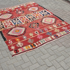 May include: A red, blue, and white patterned rug with a geometric design. The rug has a fringe border.