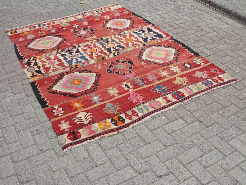 May include: A red, blue, and white patterned rug with a geometric design. The rug has a fringe border.