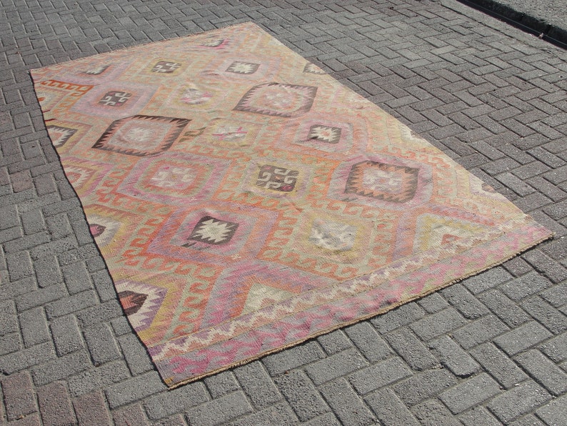 K&ouml;nnte beinhalten: Ein antiker t&uuml;rkischer Teppich mit einem geometrischen Muster in Rosa-, Orange- und Beiget&ouml;nen. Der Teppich hat einen abgenutzten und verblassten Look, der ihm ein rustikales und antikes Aussehen verleiht.