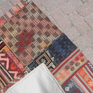 May include: A patchwork rug made of different colored fabrics with geometric patterns. The rug is made up of several smaller rugs sewn together. The rug is on a gray concrete surface.
