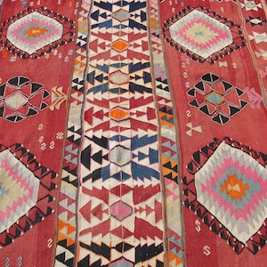 May include: A red, white, blue, and orange patterned rug with a geometric design. The rug has a traditional Turkish kilim style.