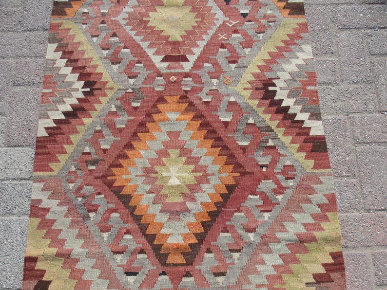 May include: A rectangular, patterned rug with a geometric design. The rug features a diamond pattern in shades of red, orange, gray, and beige. The rug is made of woven material and is suitable for use in a living room or bedroom.