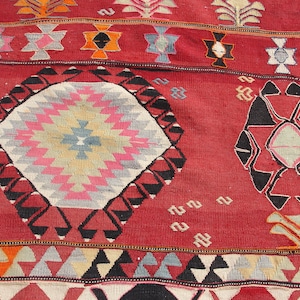 May include: A red, black, and white patterned rug with geometric designs. The rug has a central diamond shape with a starburst pattern.