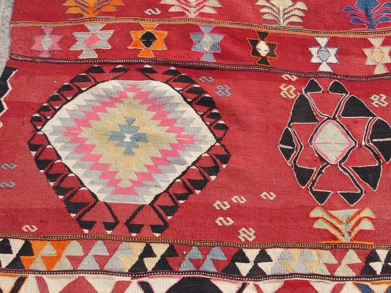 May include: A red, black, and white patterned rug with geometric designs. The rug has a central diamond shape with a starburst pattern.
