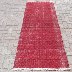 May include: A red vintage rug with a distressed look and a white fringe border. The rug has a faded, worn appearance, giving it a unique character.