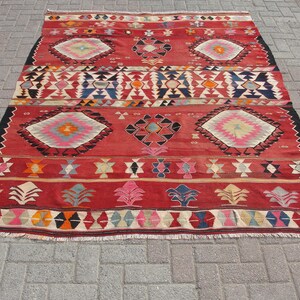May include: A red, black, and white patterned rug with geometric designs. The rug has a fringe border.