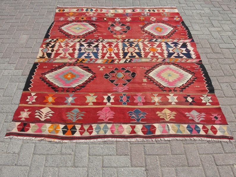 May include: A red, black, and white patterned rug with geometric designs. The rug has a fringe border.