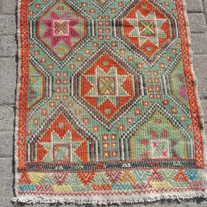 Puede incluir: Una alfombra kilim turca tradicional con un patr&oacute;n geom&eacute;trico en tonos rojos, verdes, naranjas y amarillos. La alfombra tiene un borde con flecos y est&aacute; hecha de lana.