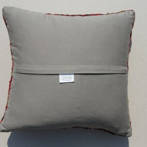 May include: The back of a square pillow with a gray fabric cover. The pillow has a zipper closure and a small white tag with text that reads "Made in Turkey".