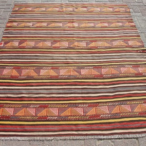 May include: A vintage striped rug with a geometric pattern in shades of red, brown, yellow, and white. The rug has a fringe border.