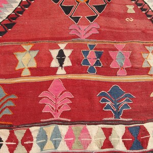 May include: Close-up of a red, blue, and white patterned rug with geometric designs. The rug has a traditional, hand-woven look.