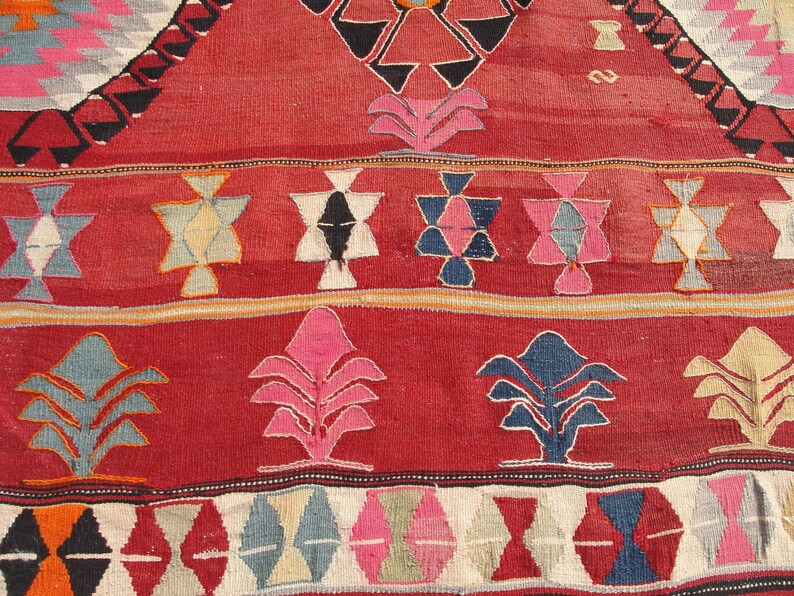 May include: Close-up of a red, blue, and white patterned rug with geometric designs. The rug has a traditional, hand-woven look.