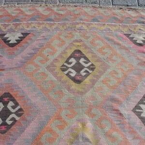 K&ouml;nnte beinhalten: Ein bunter Teppich mit einem geometrischen Muster in den Farben Rosa, Orange, Braun und Grau. Der Teppich hat ein rautenf&ouml;rmiges Design mit komplizierten Details.