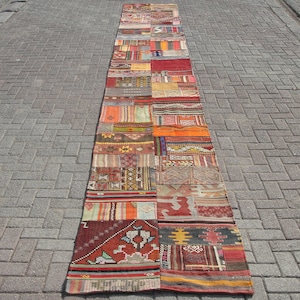 Puede incluir: Una alfombra larga y estrecha de patchwork con una variedad de colores y patrones. La alfombra está hecha de muchas piezas diferentes de tela cosidas juntas. La alfombra está colocada sobre un camino de adoquines grises.