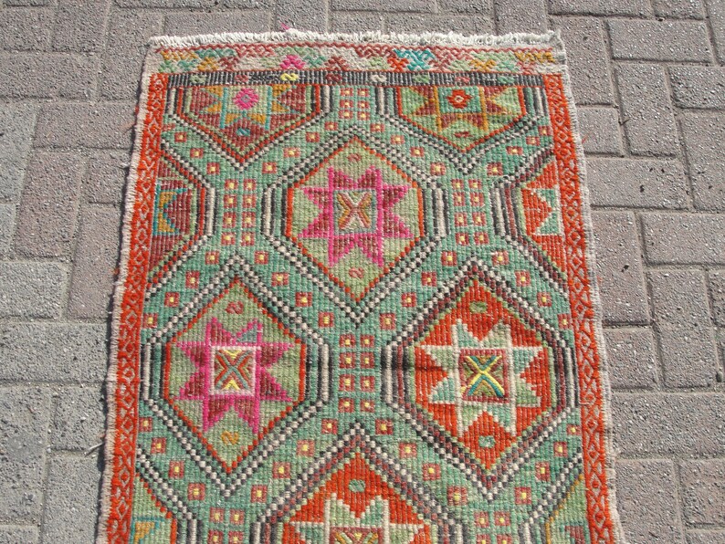 Puede incluir: Una alfombra colorida con un patr&oacute;n geom&eacute;trico en tonos rojos, verdes, naranjas y rosas. La alfombra tiene un borde de flecos.