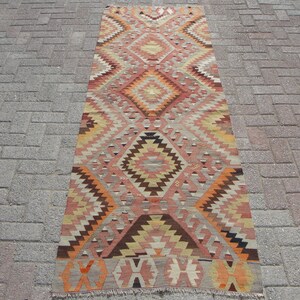 May include: A rectangular, patterned rug with a geometric design. The rug features a central diamond pattern in shades of peach, orange, brown, and cream. The rug is approximately 3 feet wide and 6 feet long.