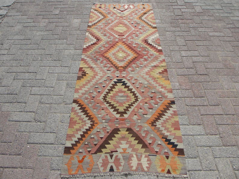May include: A rectangular, patterned rug with a geometric design. The rug features a central diamond pattern in shades of peach, orange, brown, and cream. The rug is approximately 3 feet wide and 6 feet long.