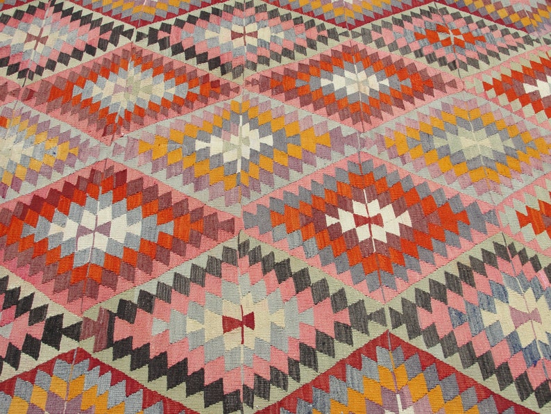 Op de afbeelding: Een kleurrijk tapijt met een geometrisch patroon in tinten rood, oranje, roze, grijs en wit.