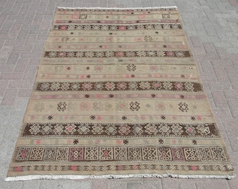 May include: A vintage rug with a geometric pattern in shades of brown, beige, and pink. The rug has a fringe border and is woven with a traditional design.