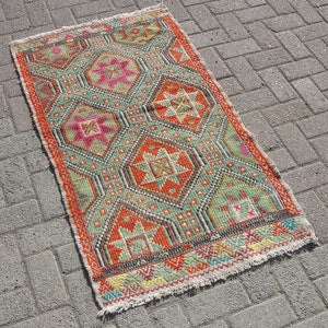 Puede incluir: Una alfombra colorida con un patr&oacute;n geom&eacute;trico en tonos rojos, naranjas, verdes y azules. La alfombra tiene un borde con flecos y est&aacute; hecha de tejido tejido.