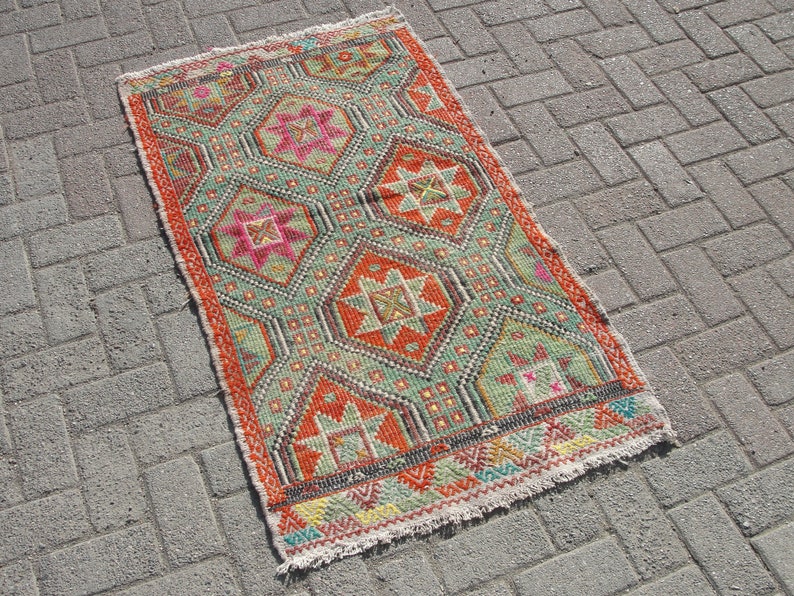 Puede incluir: Una alfombra colorida con un patr&oacute;n geom&eacute;trico en tonos rojos, naranjas, verdes y azules. La alfombra tiene un borde con flecos y est&aacute; hecha de tejido tejido.