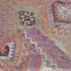 K&ouml;nnte beinhalten: Nahaufnahme eines bunten, handgewebten Teppichs mit komplizierten geometrischen Mustern in Rosa-, Lila-, Orange- und Gr&uuml;nt&ouml;nen. Der Teppich hat einen ausgefransten Rand und eine strukturierte Oberfl&auml;che.