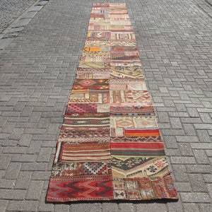 Puede incluir: Una larga alfombra rectangular de patchwork compuesta por varias piezas de tela estampada en tonos rojos, naranjas, beiges y marrones. La alfombra se exhibe al aire libre sobre una superficie de ladrillo, mostrando su longitud y diversos elementos de diseño. Aproximadamente 300 cm de largo.