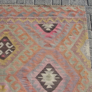 K&ouml;nnte beinhalten: Ein traditioneller t&uuml;rkischer Teppich mit einem geometrischen Muster in Braun-, Rosa-, Beige- und Gelbt&ouml;nen. Der Teppich hat einen gewebten Rand und ist aus Wolle gefertigt.