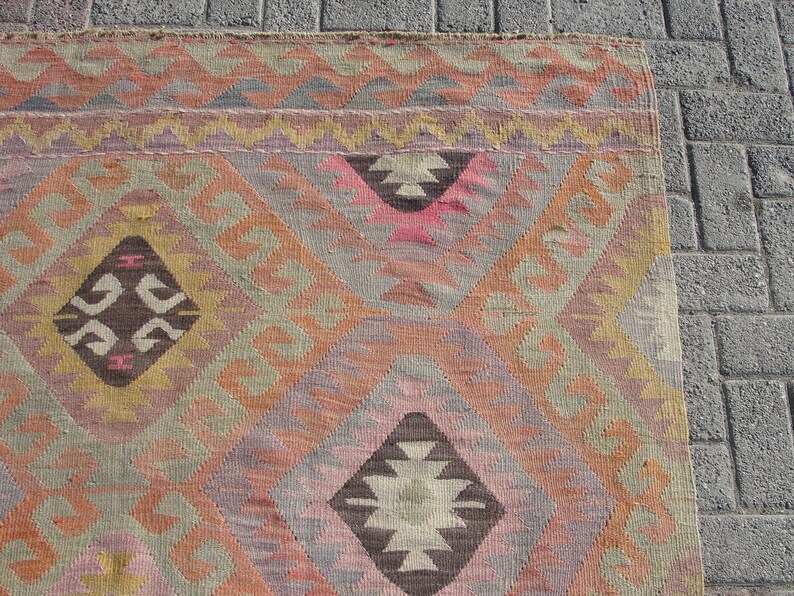 K&ouml;nnte beinhalten: Ein traditioneller t&uuml;rkischer Teppich mit einem geometrischen Muster in Braun-, Rosa-, Beige- und Gelbt&ouml;nen. Der Teppich hat einen gewebten Rand und ist aus Wolle gefertigt.