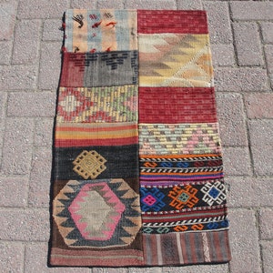 Peut inclure: Un tapis patchwork coloré avec des motifs géométriques dans des tons de rouge, marron, bleu, jaune et blanc. Le tapis est fait de tissu tissé et a une bordure frangée.