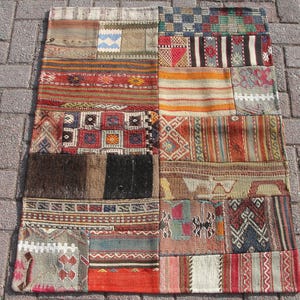 Può includere: Un tappeto patchwork con una varietà di colori e motivi, tra cui rosso, blu, verde e marrone. Il tappeto è in lana e ha una trama tessuta a mano.