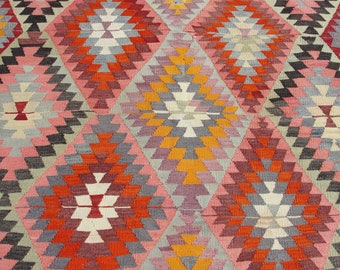 Può includere: Un tappeto colorato con un motivo geometrico in tonalità di rosa, arancio, rosso, grigio e bianco. Il motivo è composto da triangoli e rombi ripetuti.