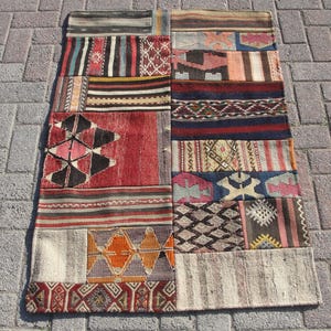 Op de afbeelding: Een patchwork tapijt met verschillende kleuren en patronen, waaronder rood, blauw, bruin en wit. Het tapijt is geweven en heeft een gefranst randje.